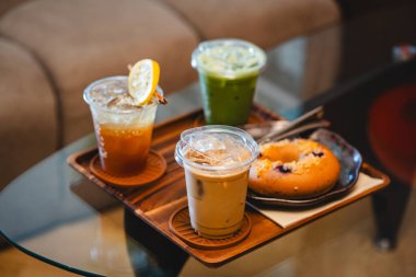 Bir bardak buzlu ballı lamon ve buzlu latte yaz terasında bir kafenin ahşap tepsisinde, menü fotoğrafçılığında..