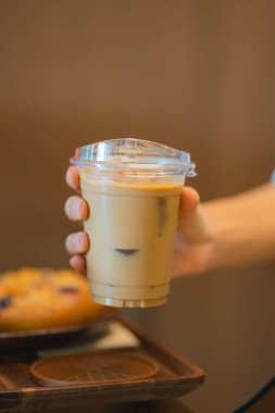 Plastik bardakta servis edilmiş buzlu latte tutan bir kadın resmi. 
