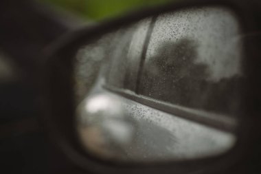 Araba yan aynasında yağmur damlaları bulanık manzarayı yansıtıyor