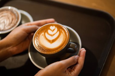 Latte tasarımlı kapuçino tutan eller.