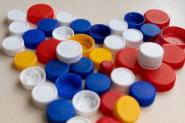 Plastik şişeleri beyaz arka planda kapatmak için kullanılan renkli vida kapakları. Plastik geri dönüşüm için kalp şeklinde kullanılmış şişe kapakları. Yüksek kalite fotoğraf