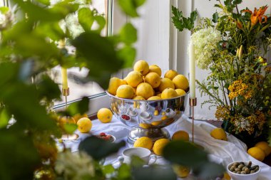 Çiçekler ve ağaç dallarıyla çevrili taze limonlarla dolu bir vazo renkli ve ferahlatıcı bir kompozisyon yaratır. Yüksek kalite fotoğraf