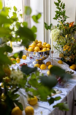  Çiçekler ve ağaç dallarıyla çevrili taze limonlarla dolu bir vazo renkli ve ferahlatıcı bir kompozisyon yaratır. Yüksek kalite fotoğraf