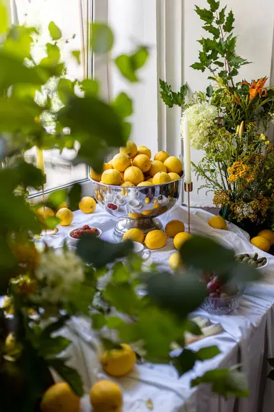  Çiçekler ve ağaç dallarıyla çevrili taze limonlarla dolu bir vazo renkli ve ferahlatıcı bir kompozisyon yaratır. Yüksek kalite fotoğraf