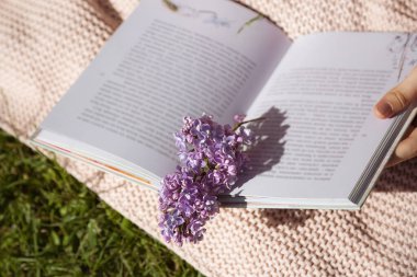 Kadının elinde içinde leylak dalı olan açık bir kitap var. Leylak bahçesinde piknik. Seçici odaklanma. Doğa. Yüksek kalite fotoğraf
