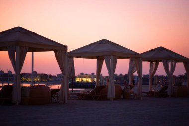 Gün batımında plaj. Deniz kenarında boş çardaklar, ertesi günü bekliyorlar.