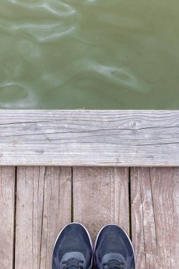 Ayakkabı ahşap bir güvertede ve küçük dalgalarla dolu bir su yüzeyinde bitiyor. Yüksek kalite fotoğraf
