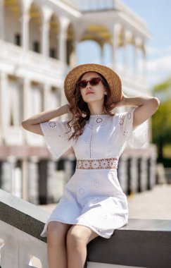 Şapkalı ve beyaz elbiseli bir kız nehir istasyonunun korkuluğunda oturuyor. Yüksek kalite fotoğraf