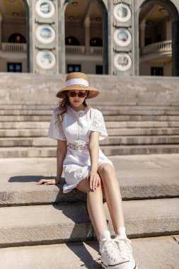Nehir istasyonunun merdivenlerinde şapkalı ve beyaz elbiseli bir kız oturuyor. Yüksek kalite fotoğraf