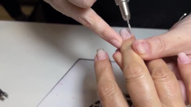 Kadın manikürcü, tırnak etlerini makineyle söküyor, yakından bakıyor. Yüksek kaliteli FullHD görüntüler