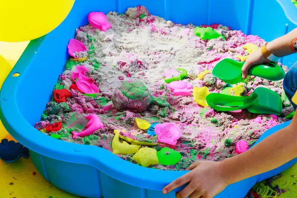 Bir çocuk kinetik kumda kürekle kazar. Fotoğrafta, çocuğun elinde kinetik kumdan yapılmış kum ve plastik oyuncaklar var. Yüksek kalite fotoğraf