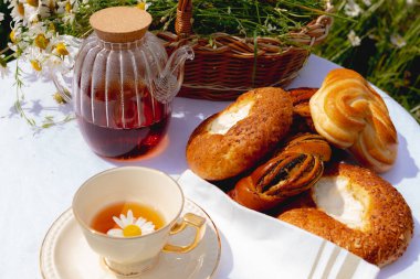 İçinde papatya çiçeği olan porselen bir fincan papatya çayı, cam bir çaydanlık ve bir sepet hamur işinin yanındaki masada yüzüyor. Yüksek kalite fotoğraf