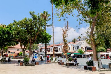 Kas, Türkiye 10 Temmuz 2025: İnsanlar marinanın yanındaki meydanda, çok sayıda kafe ve turist dükkanıyla çevrili şekilde oturuyorlar. Yüksek kalite fotoğraf