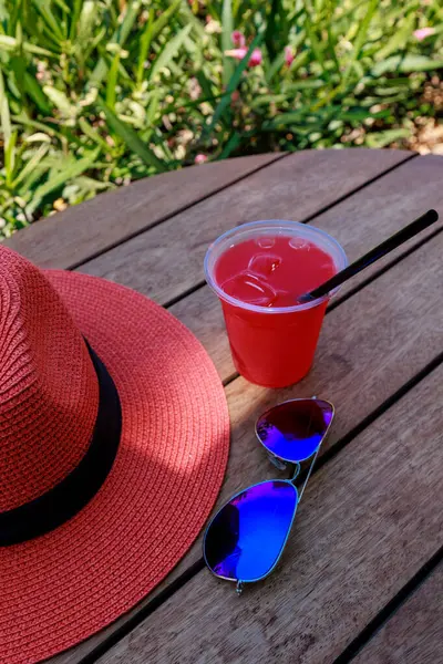 Bir bardak güneş gözlüklü ferahlatıcı kokteyl, ahşap masa üzerindeki hasır şapka mavi gökyüzü ve zakkum çalıları. Yüksek kalite fotoğraf