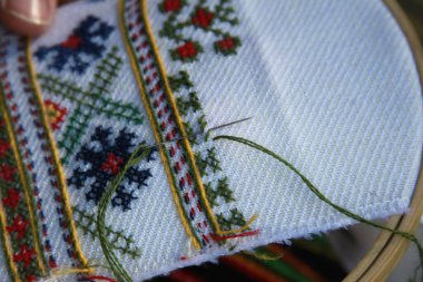 Beyaz ve kırmızı nakış tutan bir kadının eline yaklaş.