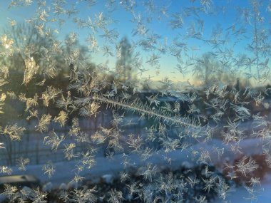 Intricate frost patterns on a window illuminated by golden sunlight, with a winter landscape and clear blue sky visible in the background, taken on a cold morning in Norway. clipart