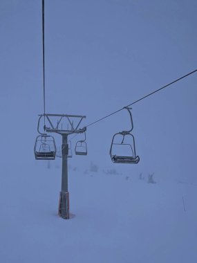 A ski lift surrounded by heavy snowfall and fog in Norefjell, Norway, with snow-covered chairs and limited visibility creating a dramatic winter scene clipart