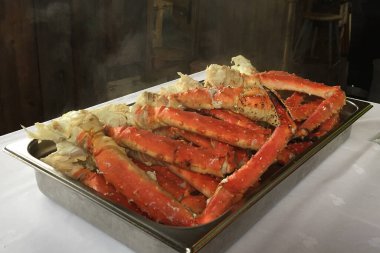 Canlı turuncu renklerini ve hassas dokularını gösteren paslanmaz çelik tepside servis edilen yeni pişirilmiş kral yengeç bacaklarının yakın plan görüntüsü. Buharın yükselmesi yeni hazırlanmış hissi güçlendirir.