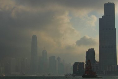 Hong Kongs skyline shrouded in heavy clouds and mist, with towering skyscrapers casting dark silhouettes over Victoria Harbour as scattered boats navigate the waters below clipart