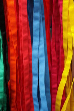 Parlak renkli kumaş şeritler dikey olarak kırmızı, mavi, sarı ve yeşil tonlarda asılı, Bangkok 'un Chatuchak Haftasonu Pazarı' nda canlı ve dokulu bir soyut desen oluşturuyor.