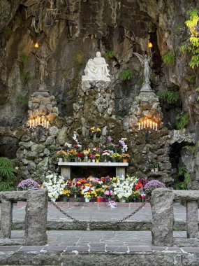 Portland, Oregon, USA - September 8, 2024: A religious shrine inside a rock grotto features a statue of the Piet angel sculptures, lit candles, and an altar adorned with colorful flowers, creating a serene atmosphere clipart