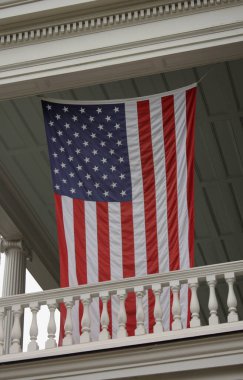 Amerika 'da dekoratif sütunları ve geleneksel mimarisi olan klasik beyaz bir balkondan sarılı büyük Amerikan bayrağı.