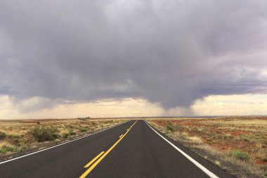 Winslow, Arizona 'nın kurak ovaları boyunca uzanan açık bir yol, ufukta görünen yağmur bulutlu bir gökyüzünün altında.