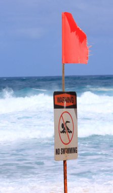 Kırmızı uyarı bayrağı ve Oahu, Hawaii 'deki Banzai Boru Hattı' nda yüzme işareti yok. Arka planda güçlü okyanus dalgaları var.