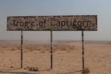 Namibya - 17 Eylül 2019: Geçen yolcuların bıraktığı çıkartmalarla kaplı kurak Namib Çölü 'nde Oğlak Tropik Çölü' nü simgeleyen yıpranmış bir yol tabelası