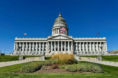 Salt Lake City, Utah, ABD - 29 Eylül 2024 Utah Eyalet Meclisi, kubbeli çatısı, simetrik kolonları ve peyzajlı bir tepede Amerikan bayrağı bulunan büyük neoklasik bir hükümet binası.