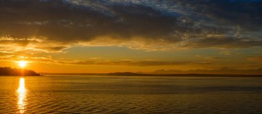 Güzel güneş kademeli olarak geniş ve geniş bir su kütlesinin üzerinde batıyor, gökyüzünü turuncu ve pembe renklerle boyuyor.