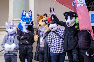 Renkli ve yaratıcı kürklü kostümler giymiş canlı bir grup neşeli bir şekilde yan yana duruyor.