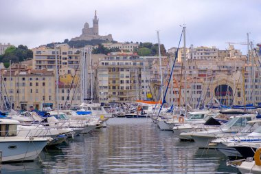 Çok sayıda tekne, pitoresk bir limana dikkatlice demirlemiştir ve hareketli bir şehrin ufuk çizgisi çarpıcı bir arka plan görevi görmektedir.