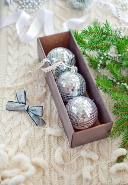 İçinde üç ayna topu, gümüş yay, gerdanlık, Noel ağacı süslemesi için kurdele ve beyaz örgü arka planda köknar dalı olan bir kutu.