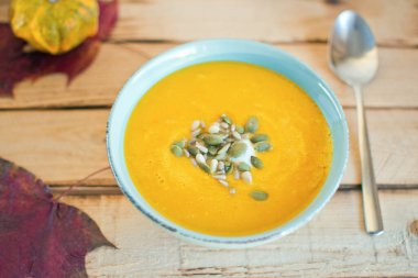 Ev yapımı balkabağı kremalı mavi kase yoğurt aromalı çorba ve kırsal ahşap masadaki tohumlar.