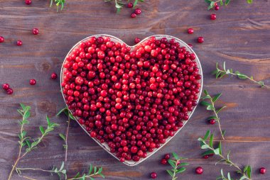 Yaban mersinli, dağ yaban mersinli ya da inek üzümlü (lat. Aşı vitis-idaea) eski ahşap bir masada kalp şeklinde bir tabakta. Etrafta bazı dallar ve böğürtlenler var.