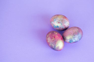 Mor arka planda galaksi renklerine boyanmış üç Paskalya yumurtası