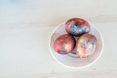 Galaksinin renklerine boyanmış üç Paskalya yumurtası beyaz tabakta.