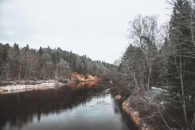 Letonya 'nın Sigulda kentindeki Gauja nehrindeki kırmızı kumtaşı mağaralarının manzarası bulutlu bir kış günü