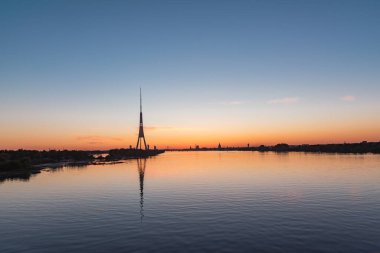 Riga Panorama 'nın silueti ve televizyon kulesi yaz akşamında gün batımından sonra Daugava nehrinde yansıyor.