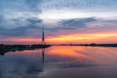 Riga Panorama 'nın silueti ve televizyon kulesi yaz akşamında gün batımından sonra Daugava nehrinde yansıyor.