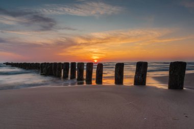 Letonya 'nın Bernati kentinde, denizden sarkan eski ahşap dalgakıran direkleriyle Baltık kıyılarında gün batımı. Uzun pozlu fotoğrafçılık.