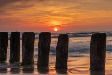 Letonya 'nın Bernati kentinde, denizden sarkan eski ahşap dalgakıran direkleriyle Baltık kıyılarında gün batımı. Uzun pozlu fotoğrafçılık.