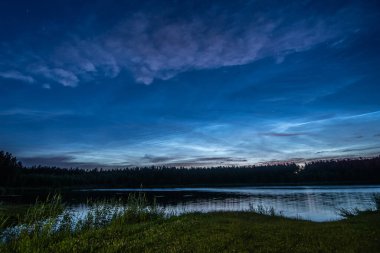 Temmuz gecesi Letonya 'daki orman gölünün üzerindeki gece bulutları