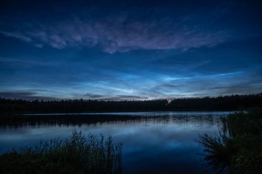 Noctilucent clouds over the forest lake in Latvia on July night clipart