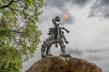 Krakow, Polonya - 23 Mayıs 2025: Wawel Ejderhası (Polonyaca: Smok Wawelski) bronz heykeli bulutlu bahar gününde ağzından ateş salıyor.