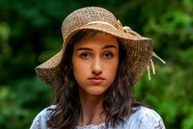 Yazlık şapkalı ve mavi bluzlu neşeli gülüşlü genç bir kadın doğanın tadını çıkarıyor..