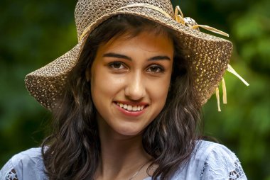 Yazlık şapkalı ve mavi bluzlu neşeli gülüşlü genç bir kadın doğanın tadını çıkarıyor..