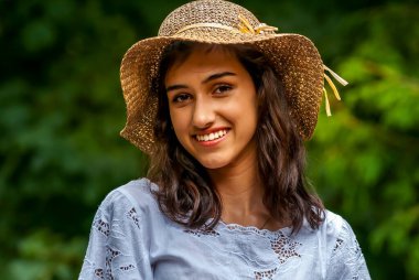 Yazlık şapkalı ve mavi bluzlu neşeli gülüşlü genç bir kadın doğanın tadını çıkarıyor..