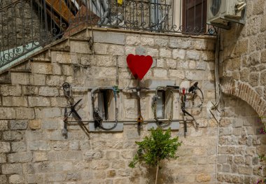 A rustic stone wall adorned with metal decorations, featuring a vibrant red heart, and a small green tree in the foreground, evoking charm and character in an outdoor setting. clipart